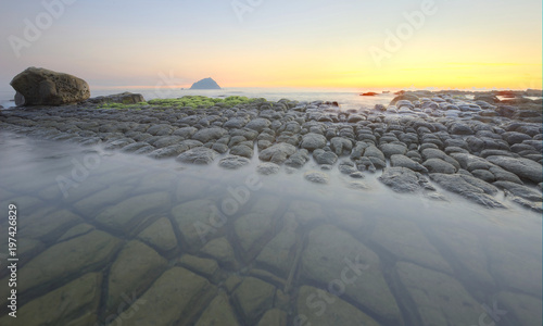Beautiful sunrise scenery at a rocky beach with unique tofu-like rock formations along the coast in northern Taiwan   an island on the distant horizon under dramatic dawning sky  long exposure effect 