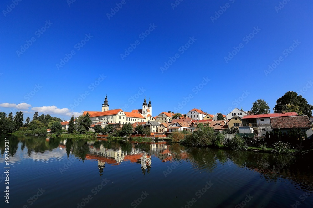 A fairy tale castle and old town with beautiful mirror reflections on smooth lake water under clear blue sky in Telc, a UNESCO world heritage site in Czech Republic, Europe 
