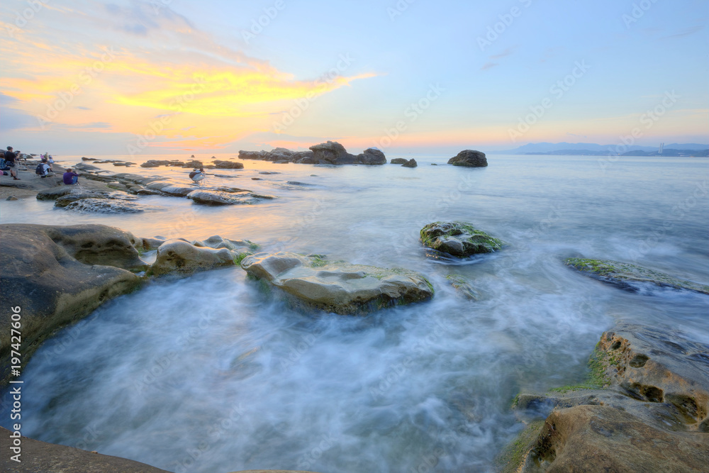Dramatic dawning sky with golden clouds over the rocky coast ~ Scenery of rising sun illuminating the sea water at a rocky beach ( Long Exposure Effect )