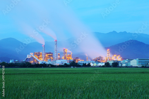 Принти на полотні View of a factory in the middle of a green farmland in the early morning twiligh
