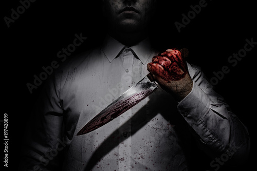 Fototapeta Photo of a killer in white shirt holding a bloody knife on black background with upper lighting