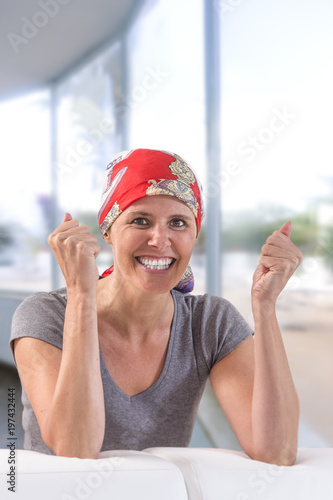 Elegant oncology middle aged patient with headscarf leaning on a table in a spacious living room with large bay windows photo