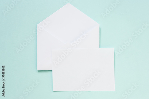 Envelope and blank paper on a pastel blue background. Mock up, top view