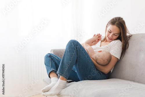 Mother is breastfeeding her kid sitting against light window background. Mom is suckling baby boy at home photo