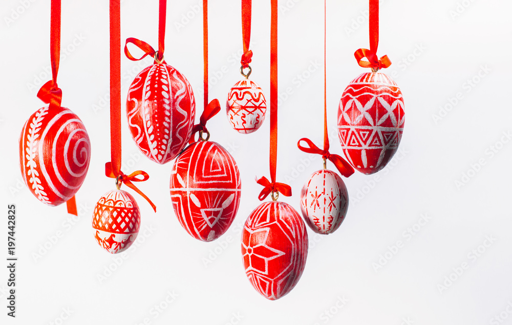 Red easter eggs with folk Ukrainian pattern hang on red ribbons from left side on white background. Ukrainian traditional eggs pisanka and krashanka. - obrazy, fototapety, plakaty 