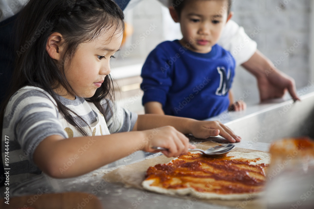 ピザ生地にソースを塗っている子供。女の子。