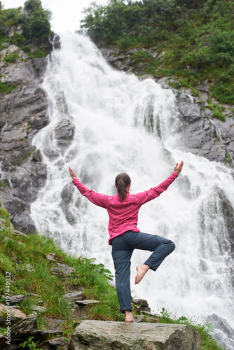 Vertical shot of a female hiker practiving yoga in front of the beautiful Balea waterfall in Fagarash mountains calamity concentration balance health vitality travelling nature tourism camping.