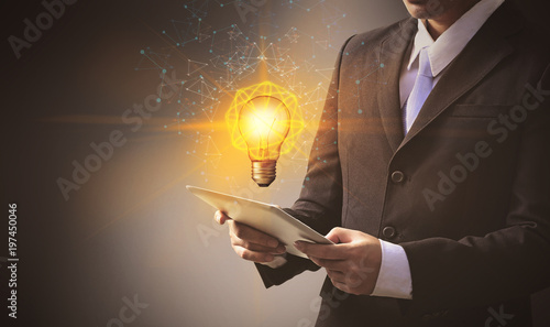 Business people working on tablet technology with floating light bulbs on top. photo