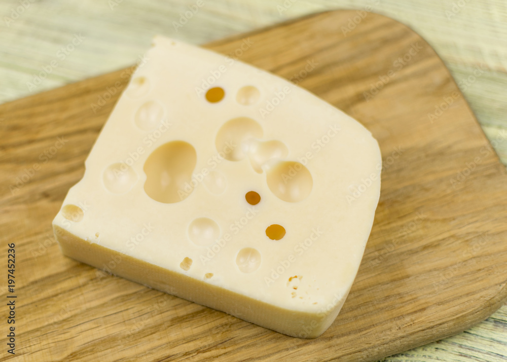 A piece of cheese with large holes on a wooden cutting board. A piece of cheese with large holes on a wooden cutting board.