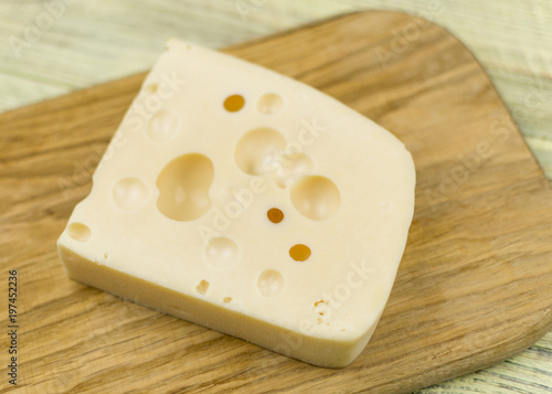 A piece of cheese with large holes on a wooden cutting board.