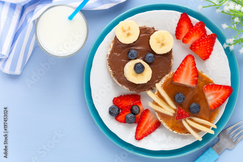 Fun food for kids - cute animal faces on crackers with chocolate and caramel spread decorated with fresh fruits - bananas, strawberries and blueberries for breakfast