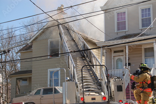 firemen fighting a roof fire on a quiet neighborhood street