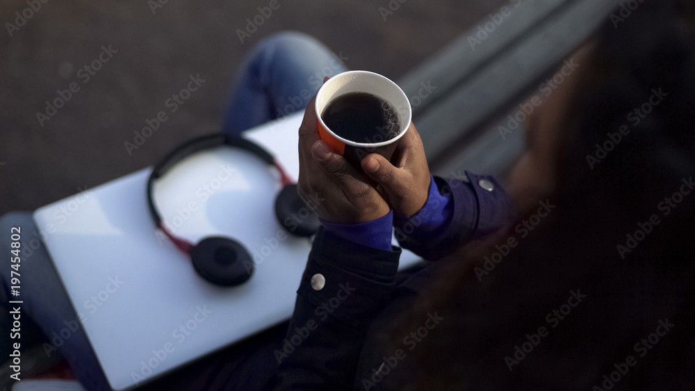 Woman warming hands, holding cup with fragrant hot drink while sitting outdoors Woman warming hands, holding cup with fragrant hot drink while sitting outdoors