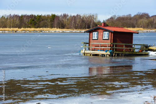 Moored floating sauna in thawing ice. Forest on opposite shore.