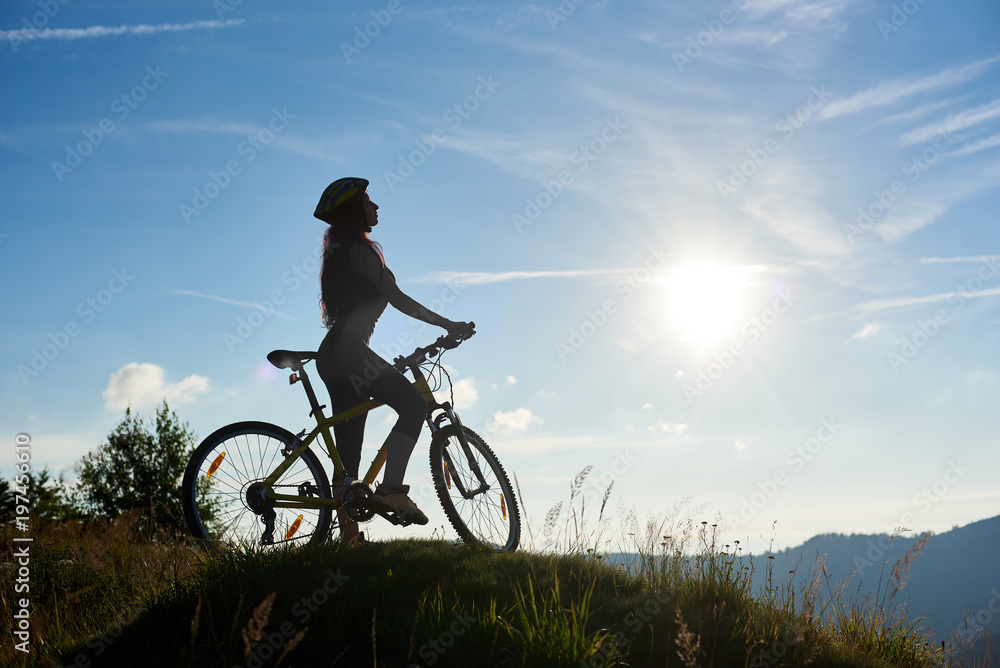Silhouette of sporty girl cyclist riding on bicycle in the mountains, wearing helmet, enjoying sunrise on sunny morning. Outdoor sport activity, lifestyle concept. Copy space Silhouette of sporty girl cyclist riding on bicycle in the mountains, wearing helmet, enjoying sunrise on sunny morning. Outdoor sport activity, lifestyle concept. Copy space