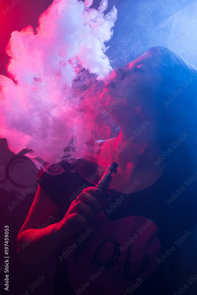 Young beautiful brunette woman with fashion makeup at the bar with a with vapor from electronic cigarette