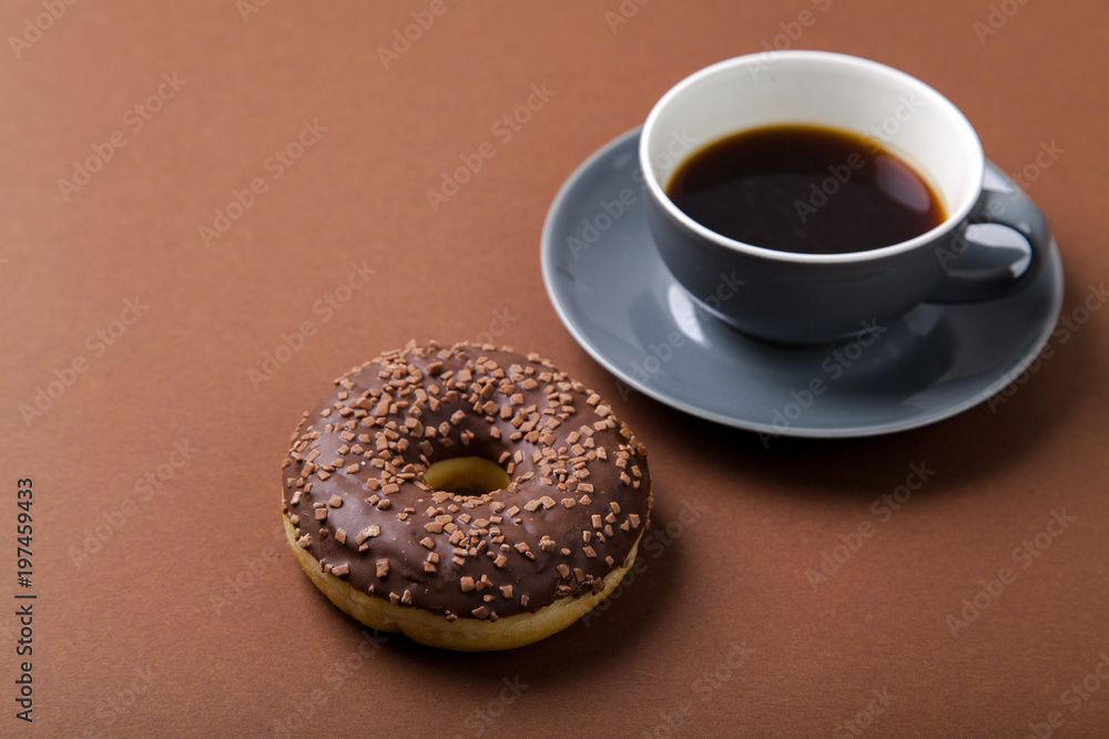 Chocolate donut and cup of black coffee on brown background. Monochromatic concept.