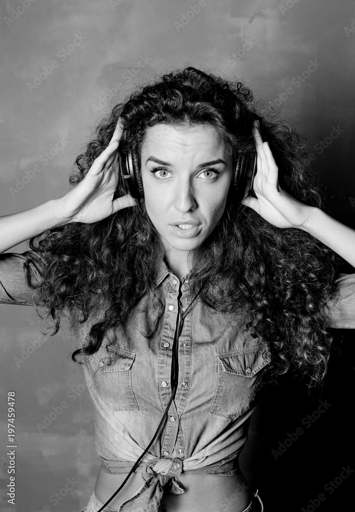 Black and white vertical studio close up portrait of attractive young Caucasian woman listening to music using big headphones, dancing and laughing. Authentic shot of lady wearing denim shirt.