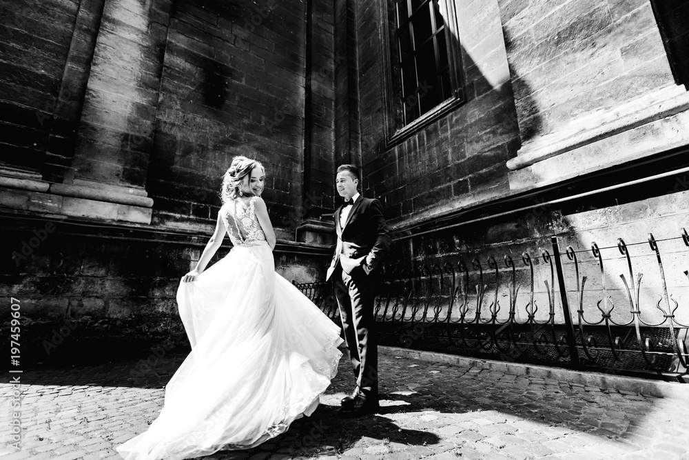 the bride dances and the groom looks at her. man holds his hands in his pockets on black and white photography the bride dances and the groom looks at her. man holds his hands in his pockets on black and white photography
