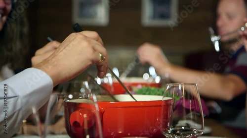 People enjoying a swiss fondue in a chalet. Fondue of melted cheese and bread. Cheerful atmosphere