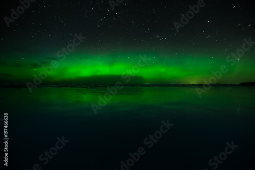 Night sky view of beautiful green aurora borealis  northern polar lights  in Finland with reflection on the frozen lake during geomagnetic storm at expedition