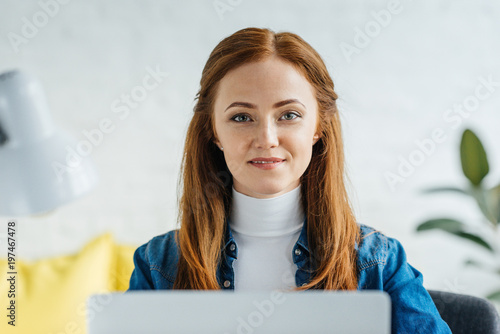 Smiling young woman looking at camera by laptop