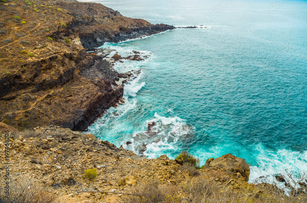 The blue waters of the Atlantic Ocean flowing into rocky cove off the coast of Tenerife.rocky coast of Canary Islands. The blue waters of the Atlantic Ocean flowing into rocky cove off the coast of Tenerife.rocky coast of Canary Islands.