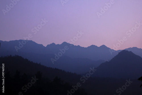 Sun-set moment, scenery of mountains in layers, dark violet purple silhouette panoramic view