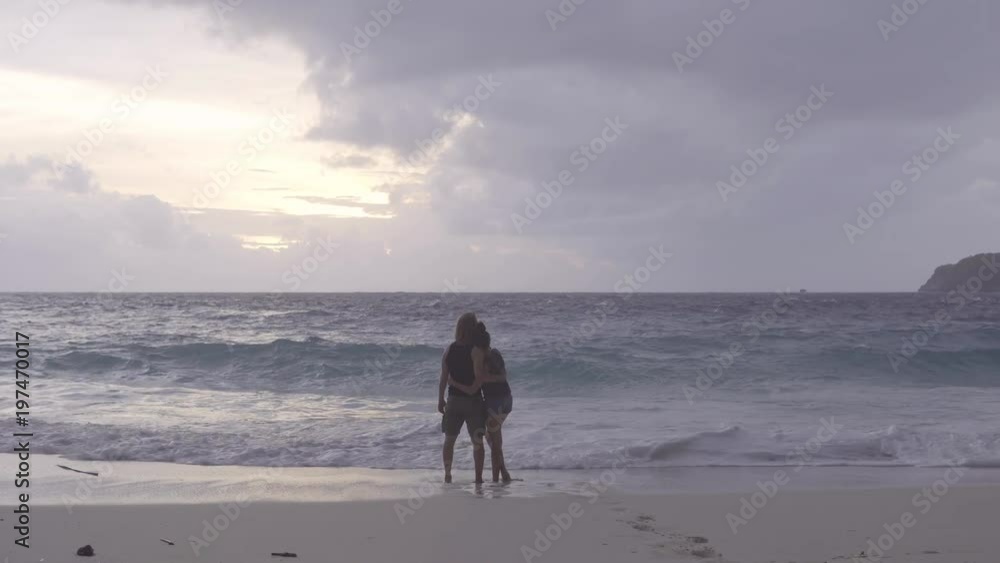 Man and woman standing near the sea, watching the sunset and hugging Man and woman standing near the sea, watching the sunset and hugging