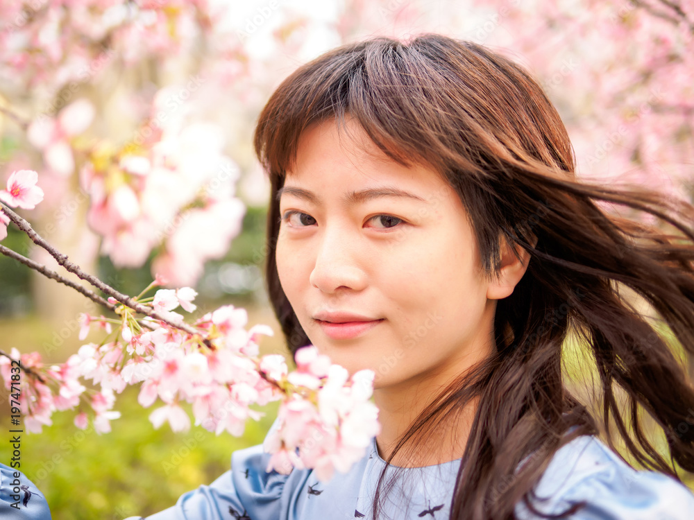Outdoor portrait of beautiful young Chinese girl in blue dress smiling among blossom cherry tree brunch in spring garden, beauty, summer, emotion, expression and people concept.