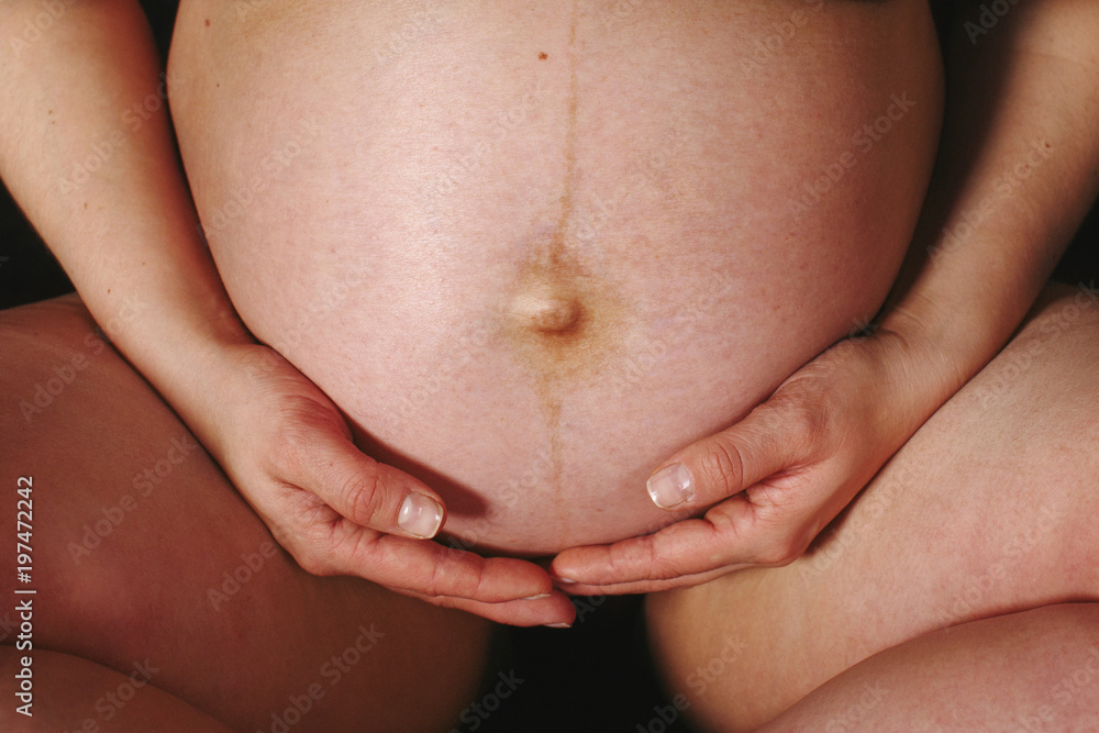 Pregnant woman hugging her belly against a black background