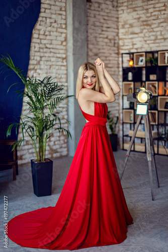 Beautiful blonde woman in red evening dress in background loft interior. Fashion photo shoot © demchyna