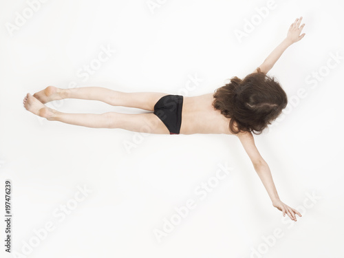 Unusual little boy in bathing suit lying on stomach with arms outstretched, isolated on light