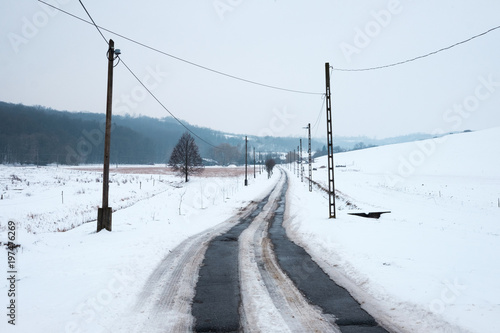 snowy winter landscape, asphalt road leads in to the hills, pylons and wires