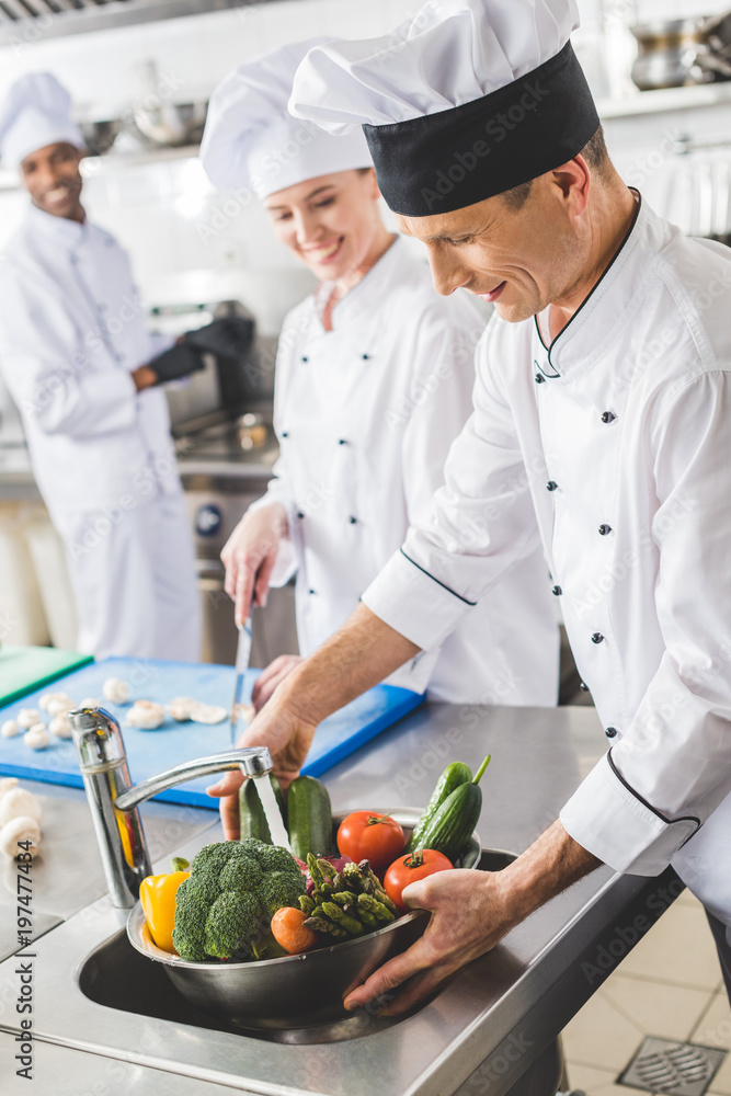 smiling chef washing vegetables at restaurant kitchen smiling chef washing vegetables at restaurant kitchen