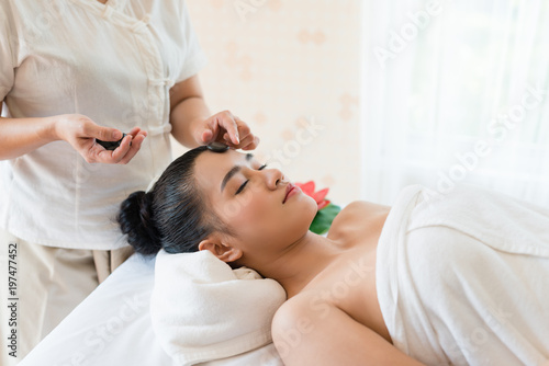 Young beautiful Asian woman relaxing having facial massage with mineral stone in the spa