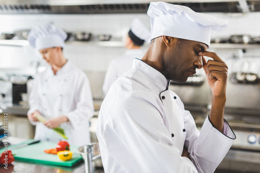 tired african american chef touching nose bridge at restaurant kitchen