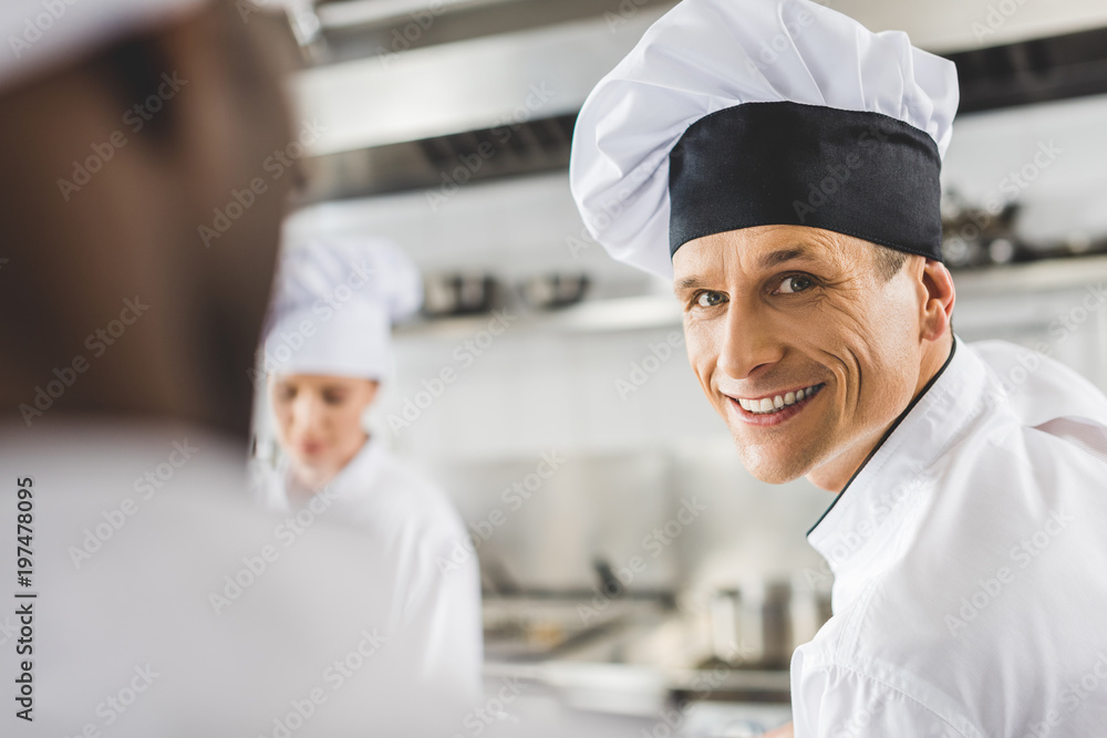 handsome smiling chef looking at camera at restaurant kitchen