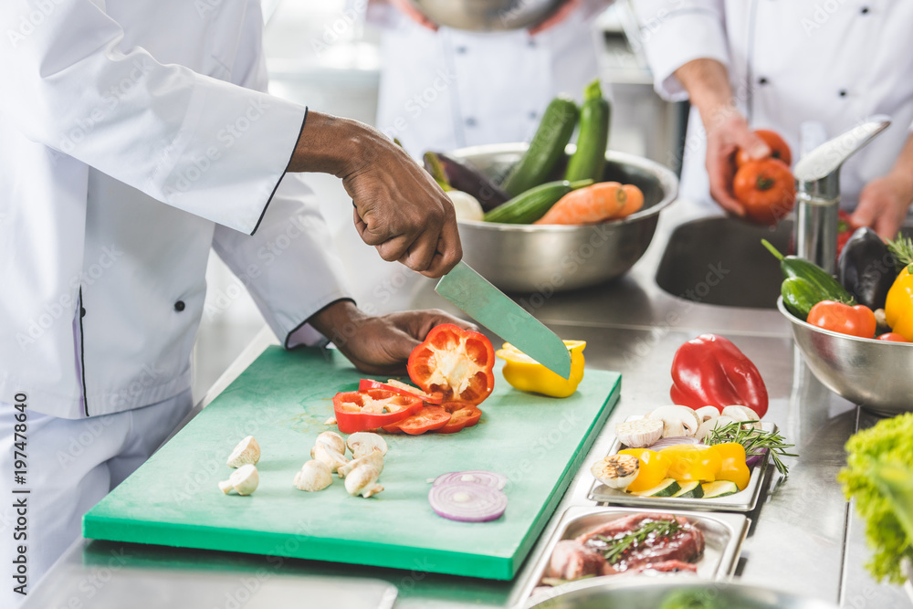 cropped image of multicultural chefs cutting and washing vegetables at restaurant kitchen cropped image of multicultural chefs cutting and washing vegetables at restaurant kitchen