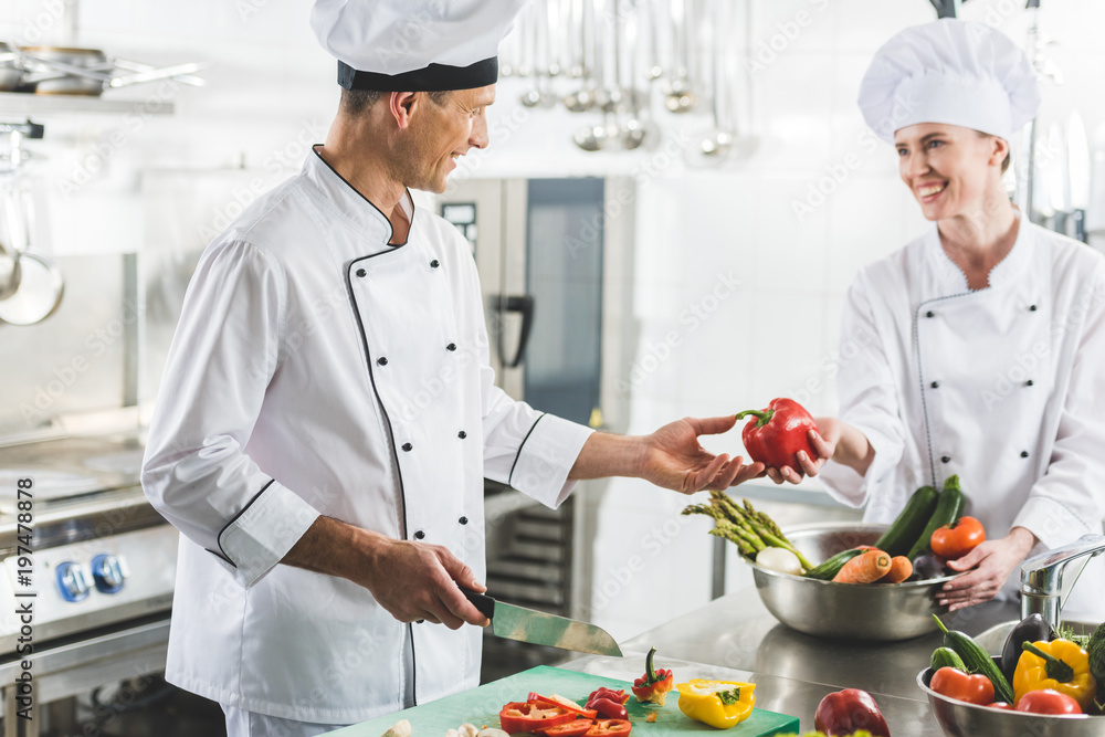 female chef giving red bell pepper to colleague at restaurant kitchen female chef giving red bell pepper to colleague at restaurant kitchen