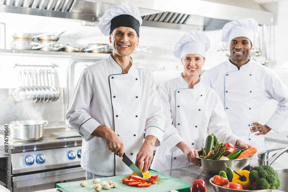 smiling multicultural chefs looking at camera at restaurant kitchen smiling multicultural chefs looking at camera at restaurant kitchen