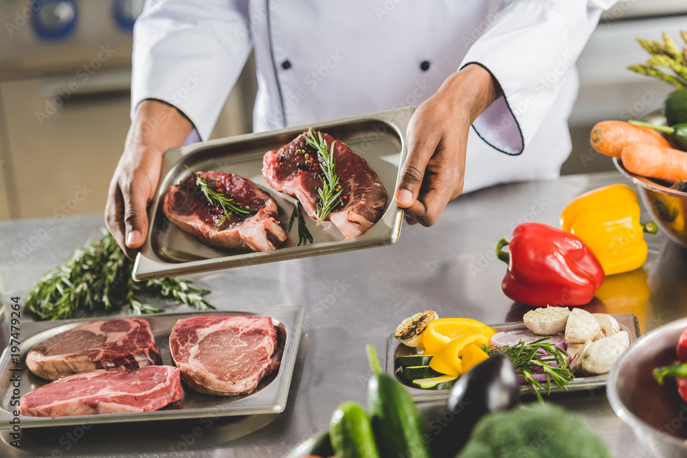 cropped image of african american chef holding tray with raw meat at restaurant kitchen