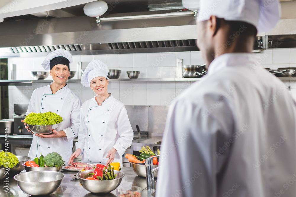 smiling multicultural chefs looking at each other at restaurant kitchen smiling multicultural chefs looking at each other at restaurant kitchen