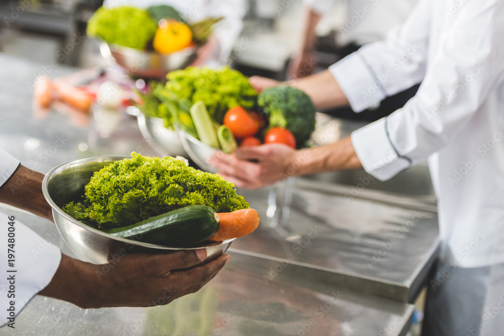 cropped image of multicultural chefs holding bowls with vegetables at restaurant kitchen cropped image of multicultural chefs holding bowls with vegetables at restaurant kitchen
