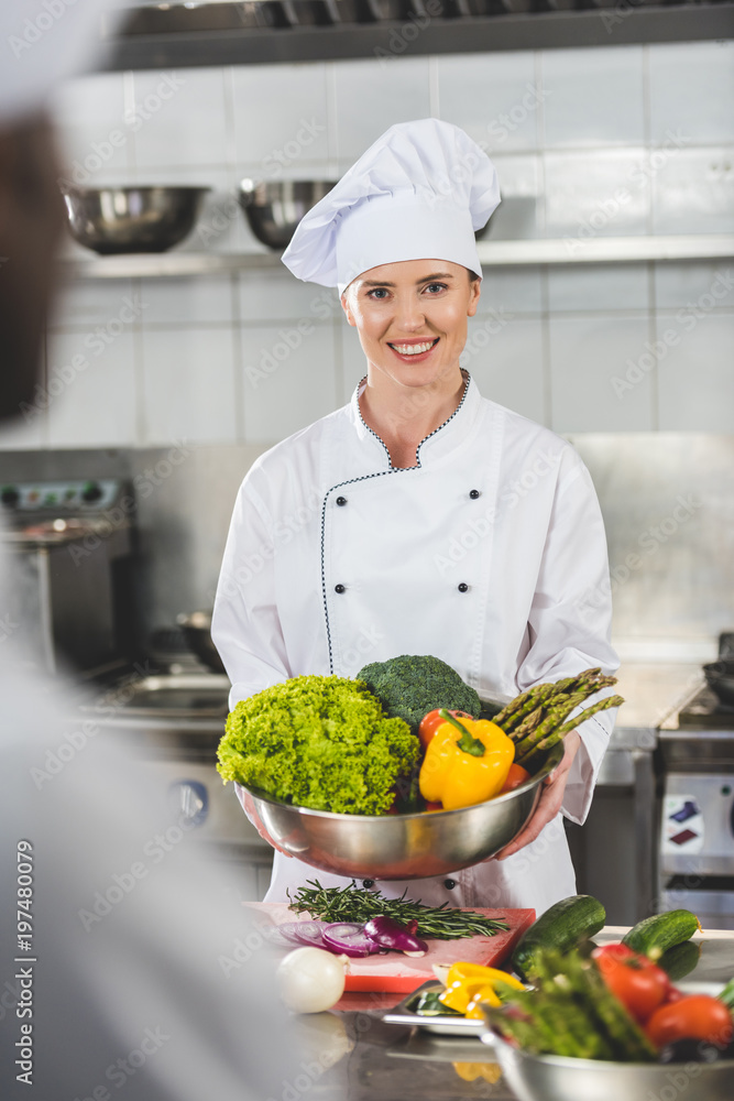 smiling chef holding bowl with vegetables and looking at camera at restaurant kitchen smiling chef holding bowl with vegetables and looking at camera at restaurant kitchen