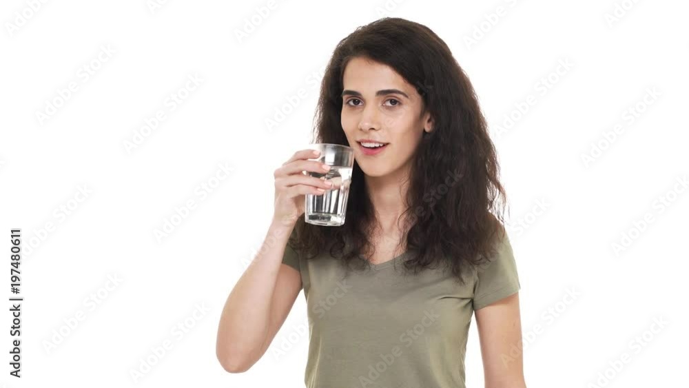 Portrait of curly haired female wearing casual t-shirt drinking water from glass and taking pleasure in fresh liquid, over white background. Concept of emotions Portrait of curly haired female wearing casual t-shirt drinking water from glass and taking pleasure in fresh liquid, over white background. Concept of emotions