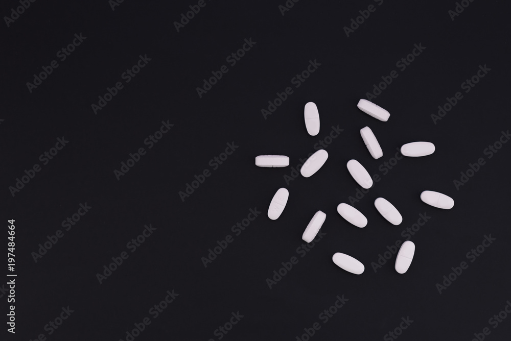 Scattered white pills on a black background with a place for text. Medical concept. Scattered white pills on a black background with a place for text. Medical concept.