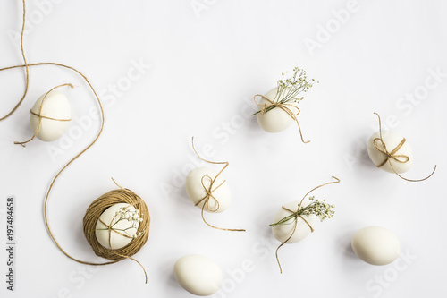 Easter eggs are minimalistically decorated with twine and gypsophila flowers. On a white background with a brown rope. Top view, flat lay photo