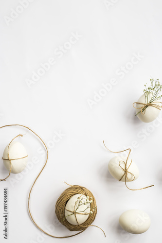 Easter eggs are minimalistically decorated with twine and gypsophila flowers. On a white background with a brown rope. Top view, flat lay photo