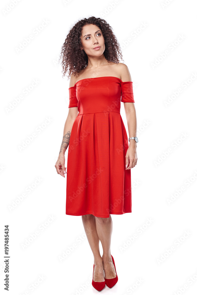 Beautiful curly female in red dress and red high heels shoes in full length looking away at blank copy space Beautiful curly female in red dress and red high heels shoes in full length looking away at blank copy space